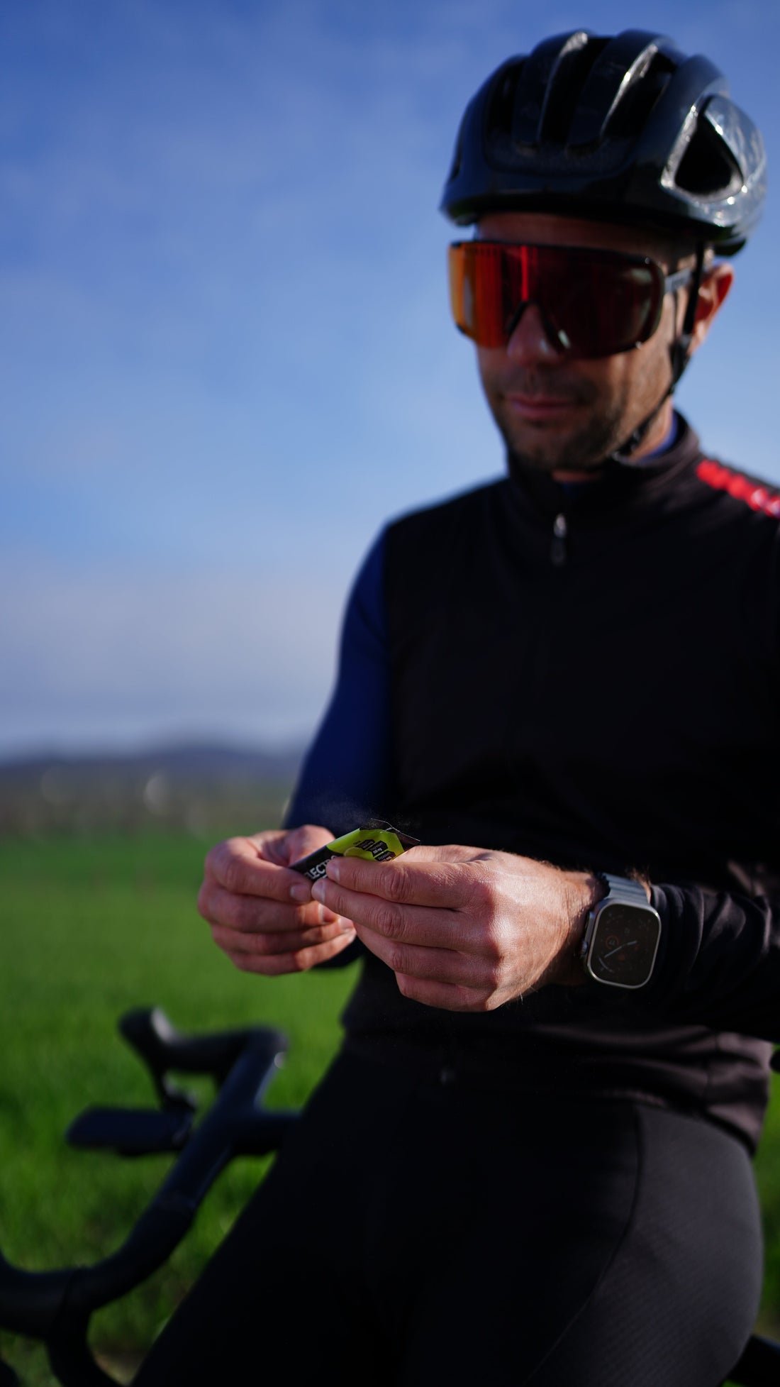 Cyclist in black gear taking COR-X electrolytes during outdoor endurance training for hydration and performance.